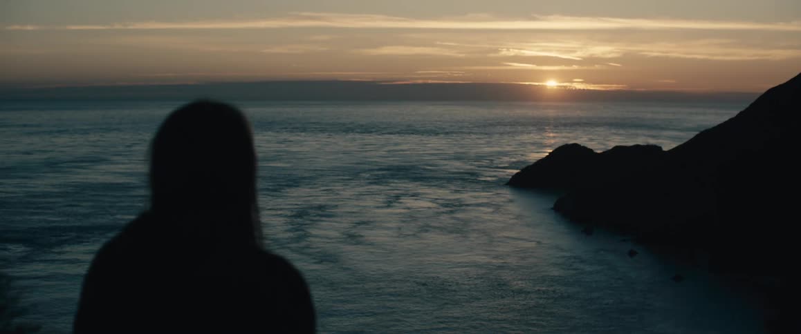A woman watches the sun set over the ocean