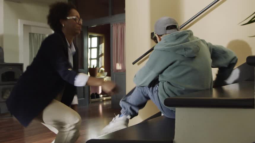 Mother tying her sons shoelaces as he stands up and picks up a backpack