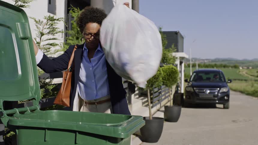 Woman taking out trash bags to trash container near front porch then walking to her car