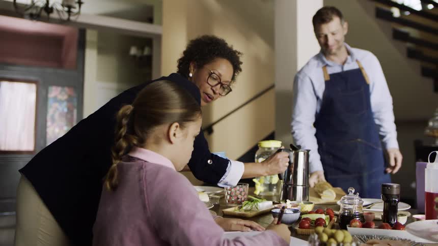A mother walks up to her daughter who is doing homework at the dinner table