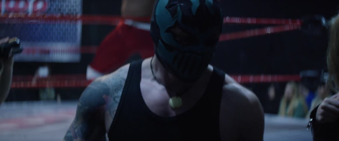 A wrestler walks past as another leans against ropes in a ring