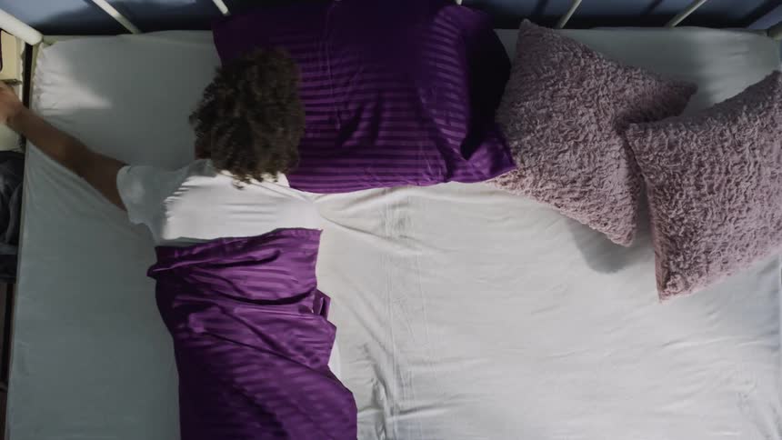 Black woman rolls and reaches while sleeping during daytime before waking up and sitting shortly after