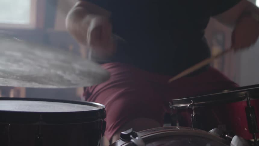 A person plays a drum kit energetically in a dimly lit room