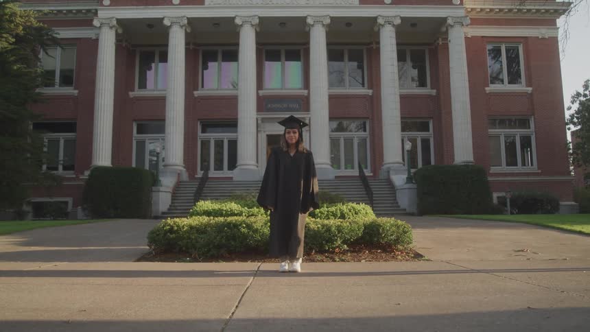 Graduate poses in front of a university building in cap and gown