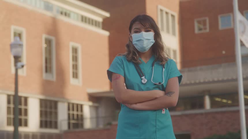 A nurse in a blue garb stands outside a large building
