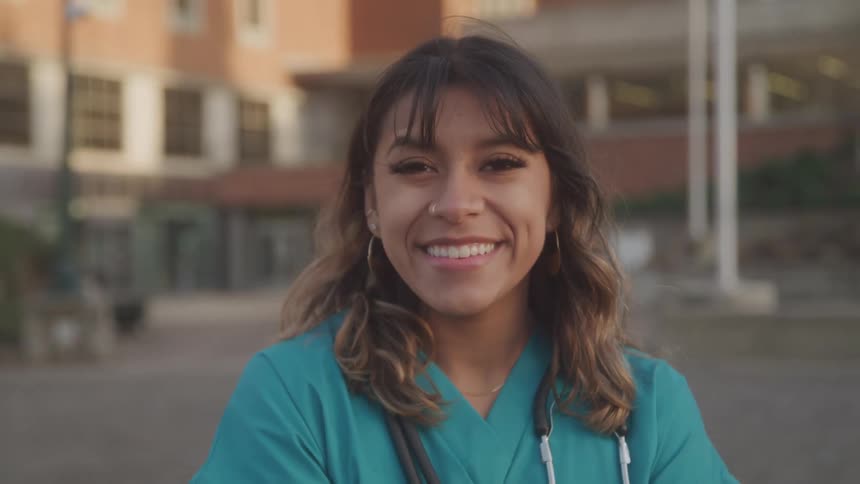 Smiling young nurse stands confidently outdoors in scrubs