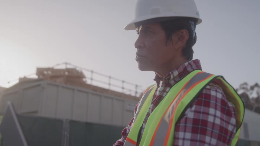 The worker is using a laptop on the construction site