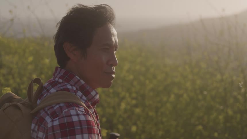A man with a backpack stands in a field of wildflowers gazing into the distance at sunset