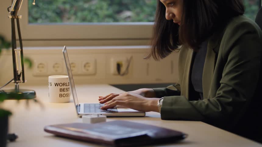 A woman sets a timer before typing on a laptop at a desk in a modern cozy office