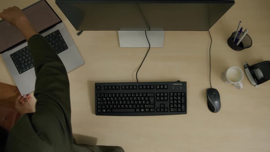 A wooden table with a keyboard and a mouse and a person placing a notebook next to it