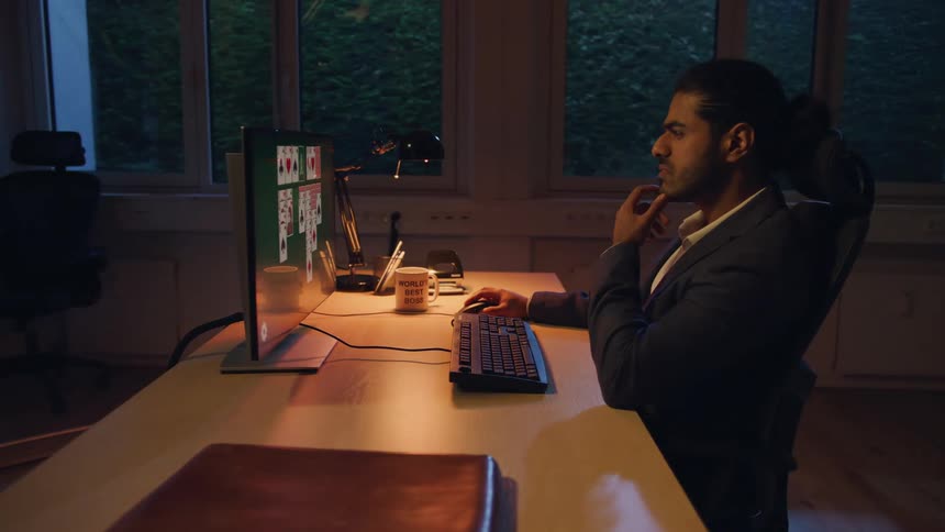 A person plays solitaire on a desktop computer in a dimly lit empty office
