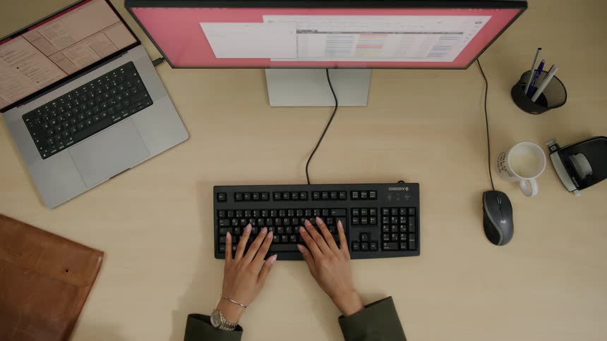 Woman working on her computer while in the office takes a sip of coffee