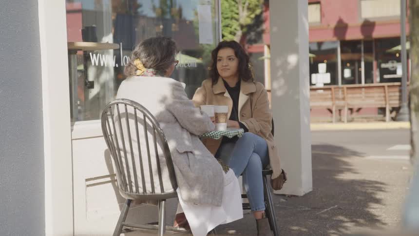 Two women have coffee together at the shops outdoor seating