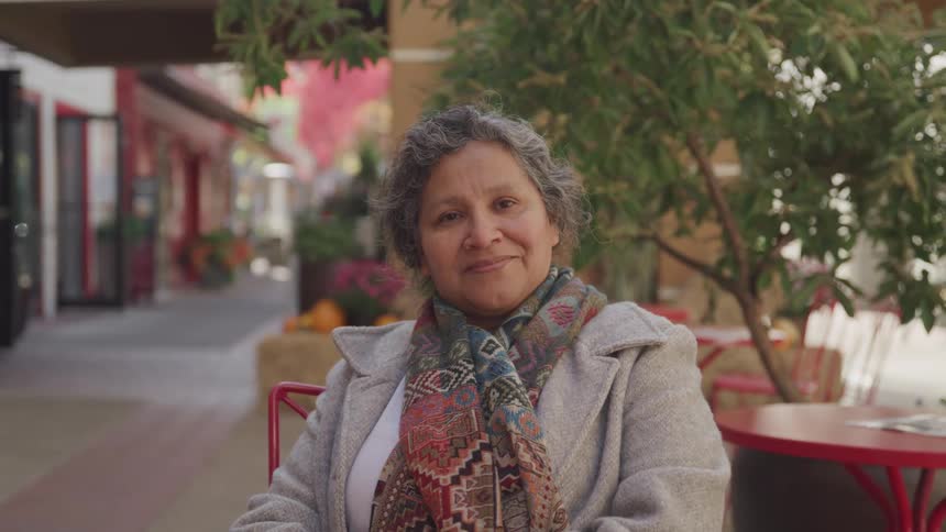 The face of a lady who has a subtle smile on her face and she is sitting on a bench on a sidewalk looking straight ahead