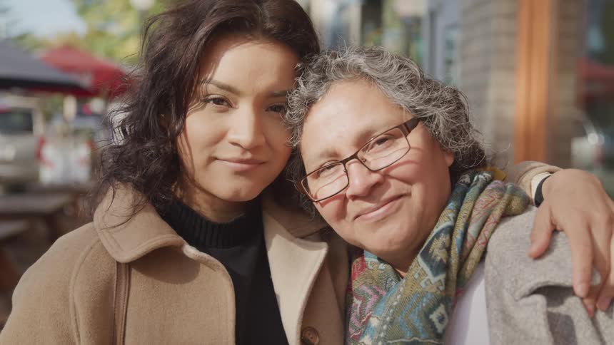 Two women hug and smile at the camera in an urban setting