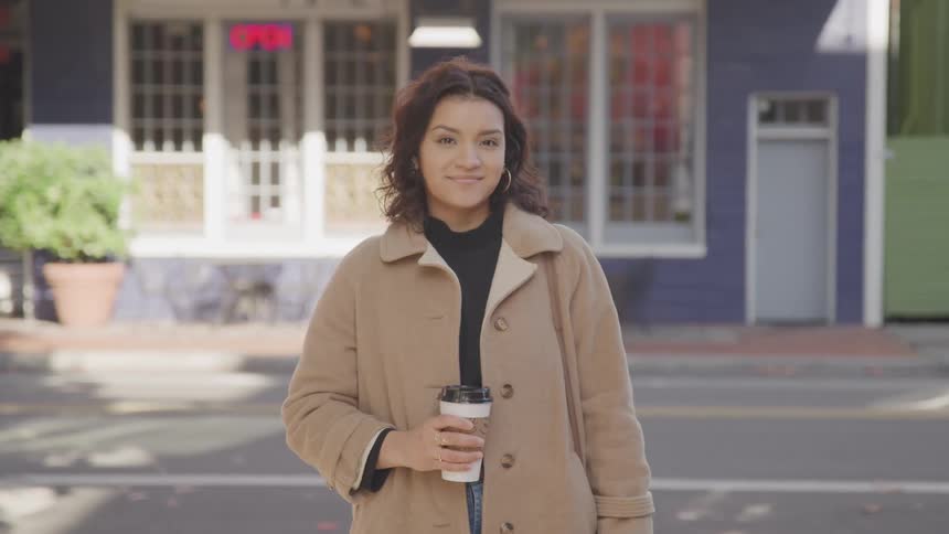 Woman in a brown coat holding a disposable coffee cup
