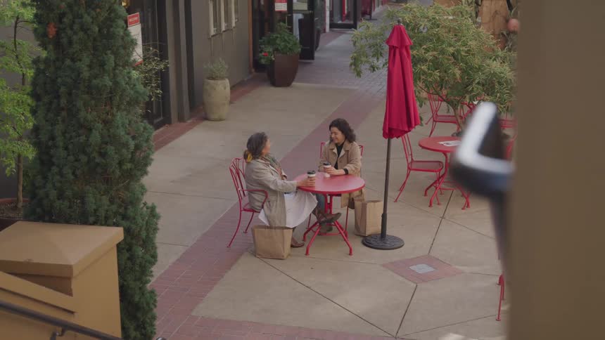 Two women are seated at a caf table outdoors engaged in a conversation on a sunny day