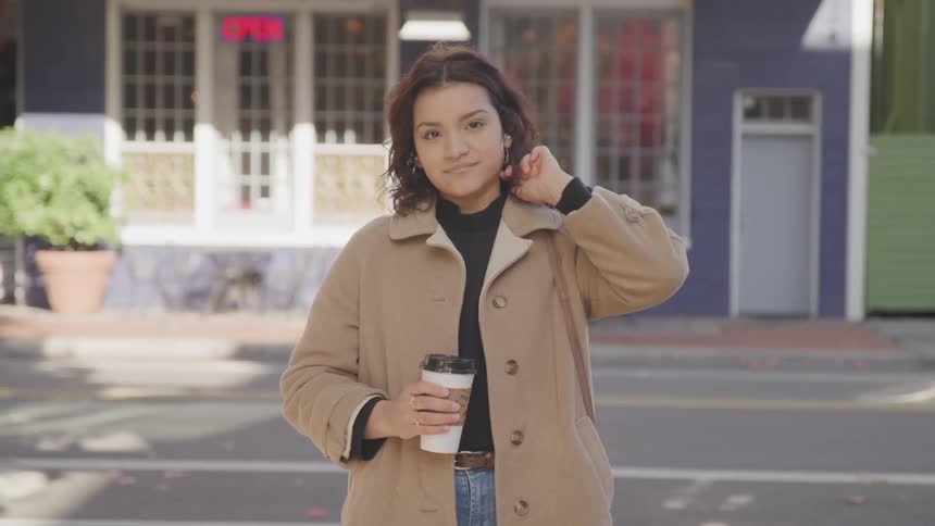 Woman standing outdoors holding a coffee cup and smiling slightly