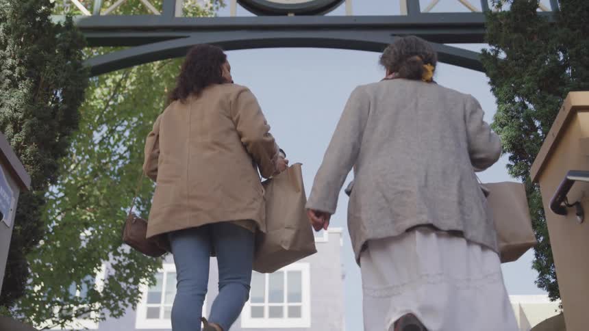 Back of two women climbing stairs unto a street while holding bags at daytime