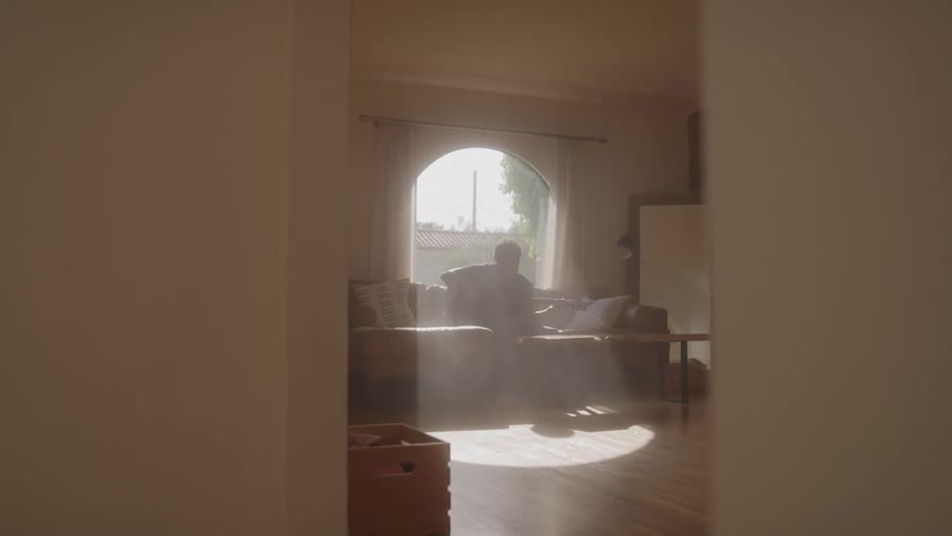 Young man plays a guitar while sitting on a couch in a room during daytime
