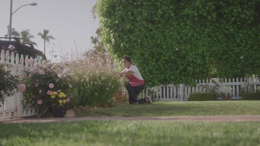 Man kneeling on the grass tending to his flower garden in the backyard