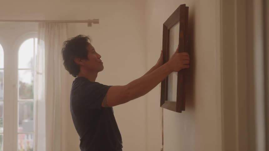 Man lifting wood picture frame to hang on interior wall