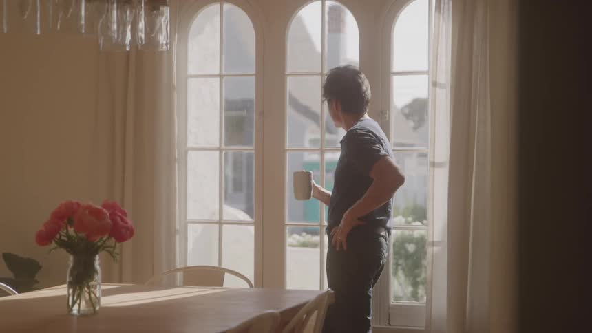 Man stands indoor near the window with a coffee mug in hand at daytime