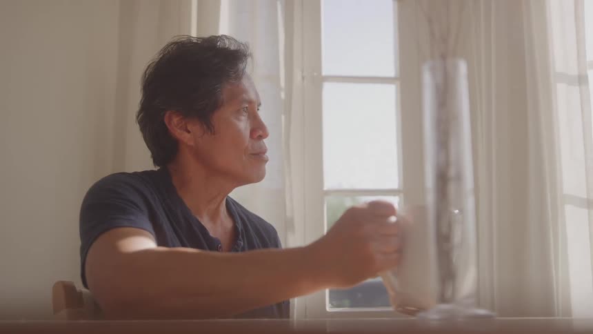 Man sitting and looking out a window drinks from a mug