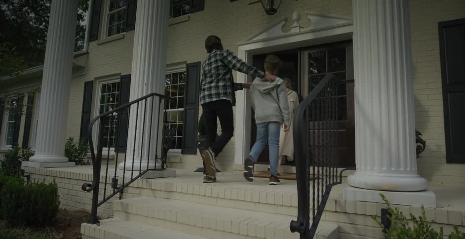 A woman wearing pajamas walks into a building followed by two of her sons around midday