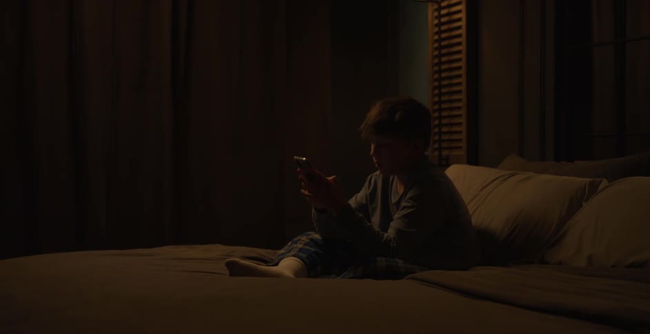 Boy sitting on bed interacting with a smartphone