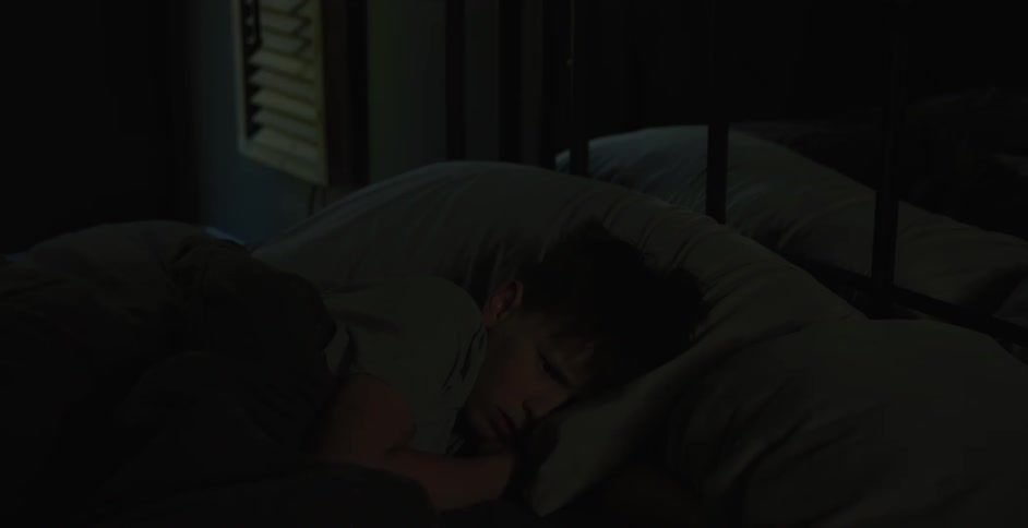A kid wakes up from bed looks at his phone and then stands up at night