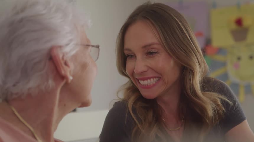 Mother and daughter sitting indoors smile at each other
