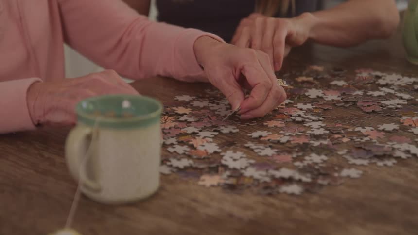 Two people are working together on a jigsaw puzzle at a wooden table