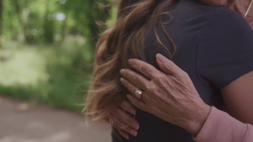 A hand with wrinkles gently touches the shoulder of another person showing a ring on a finger