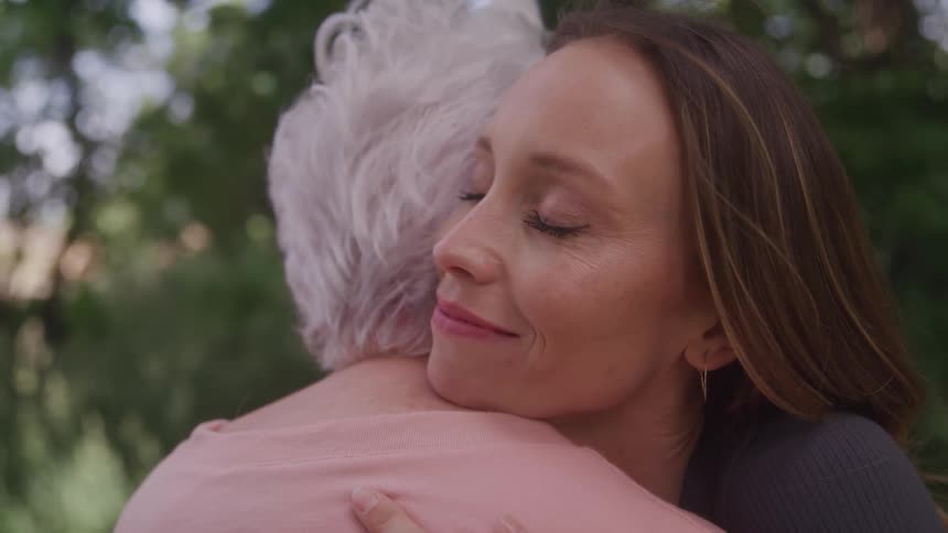 Close up of a young woman happily hugging an elderly woman as they stand outdoors during daytime