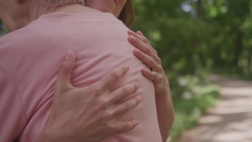 Two women in an outdoor setting of trees hugging each other affectionately