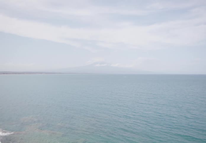 A calm ocean extends into the horizon under a partly cloudy sky