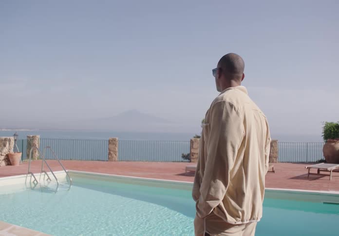 A man stands by a pool overlooking the ocean under a clear sky