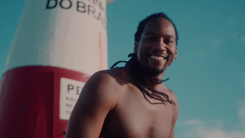 A black man with dreadlocks near a lighthouse tower smiling happily