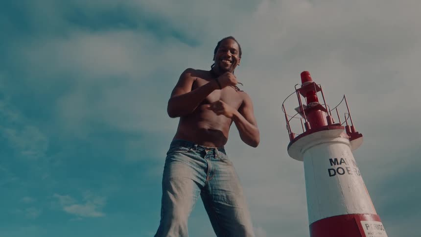 Smiling shirtless man dances in front of a lighthouse