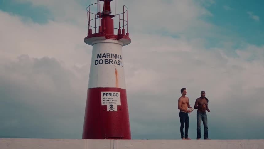 Two shirtless men wearing jeans next to a navy lighthouse