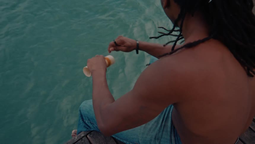 A teenage boy sits on a deck at the ocean rolling up fishing wire