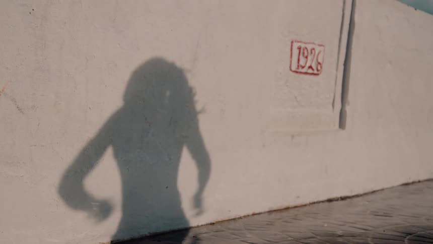 A mans shadow is seen dancing on a wall on a sunny day