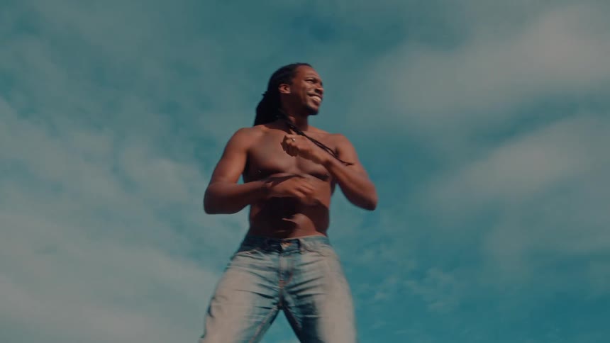 Man without a shirt and wearing jeans dancing outdoors