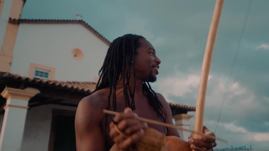 The man plays a musical instrument in front of the bell tower