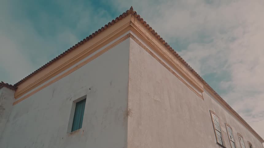 Lowangle view of a corner of a traditional stucco building with tiled roof against a partly cloudy sky