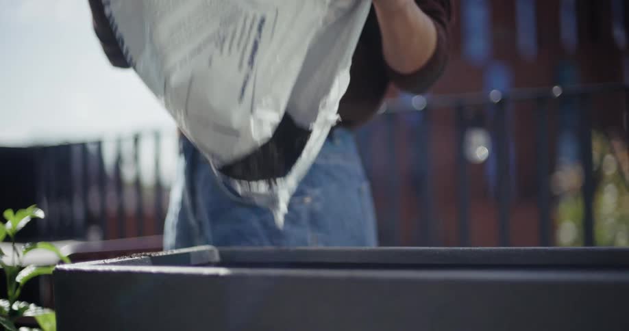 A man pouring black soil inside a rectangular container during the day