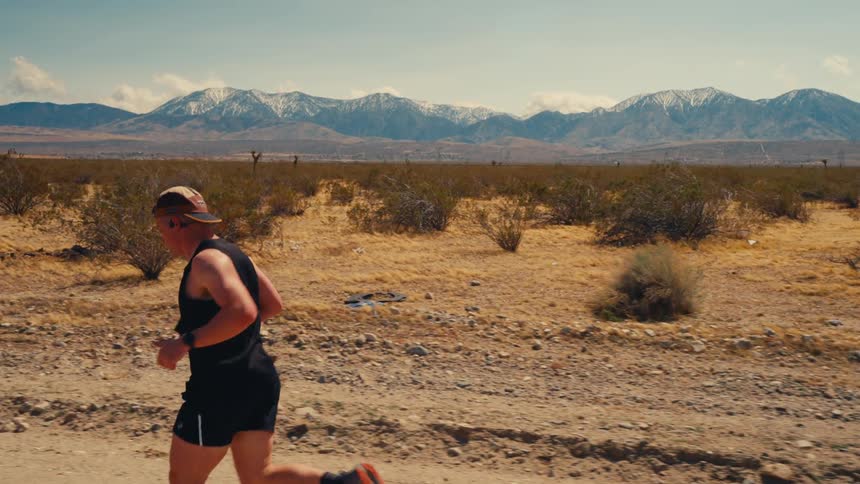 A person is running along a dirt path in a desert landscape with mountains in the background