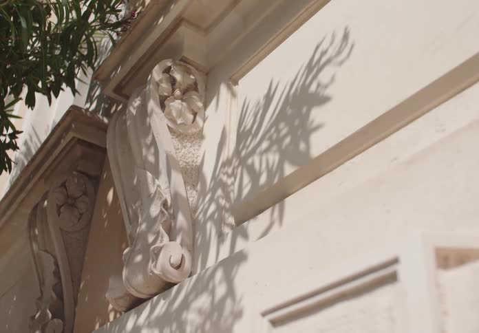 A detailed view shows an ornate white architectural element on a building with the shadow of leaves cast upon it