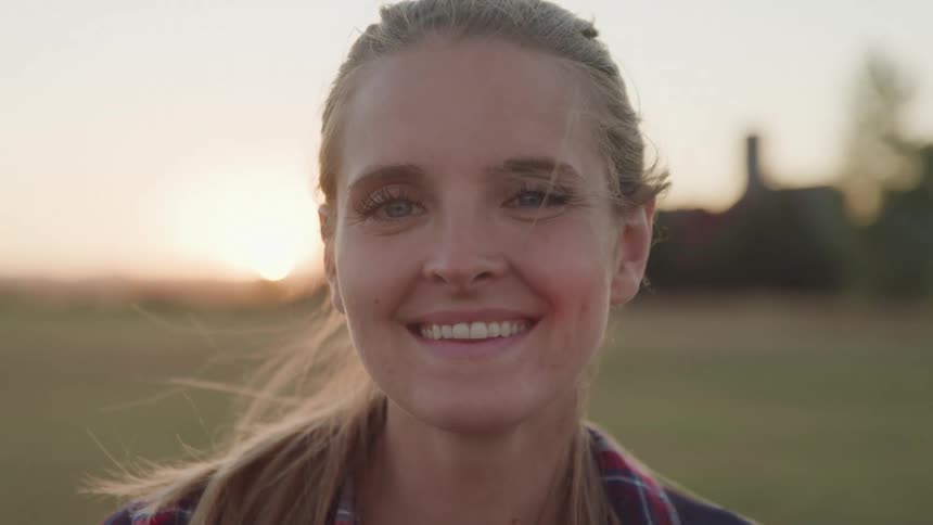 A smiling woman is shown in closeup outdoors at sunset